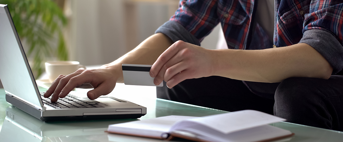 Man holding credit card, typing on laptop, paying for utilities, shopping online.