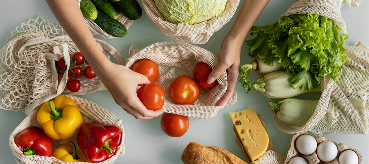 Woman's hand, holding a reusable grocery bag with vegetables on a kitchen at home and takes tomato out. 
