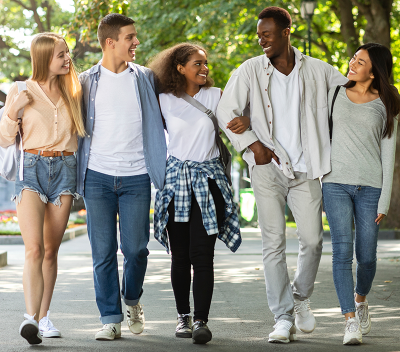 Happy students walking together in public park.