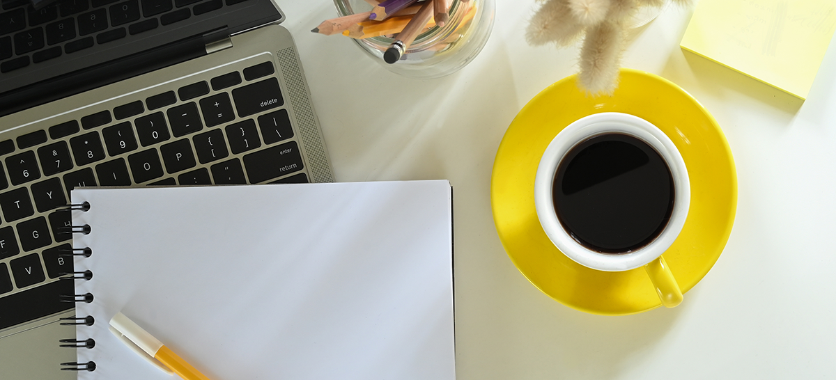 A laptop, empty notebook, a pen, and a cup of coffee on top of table.