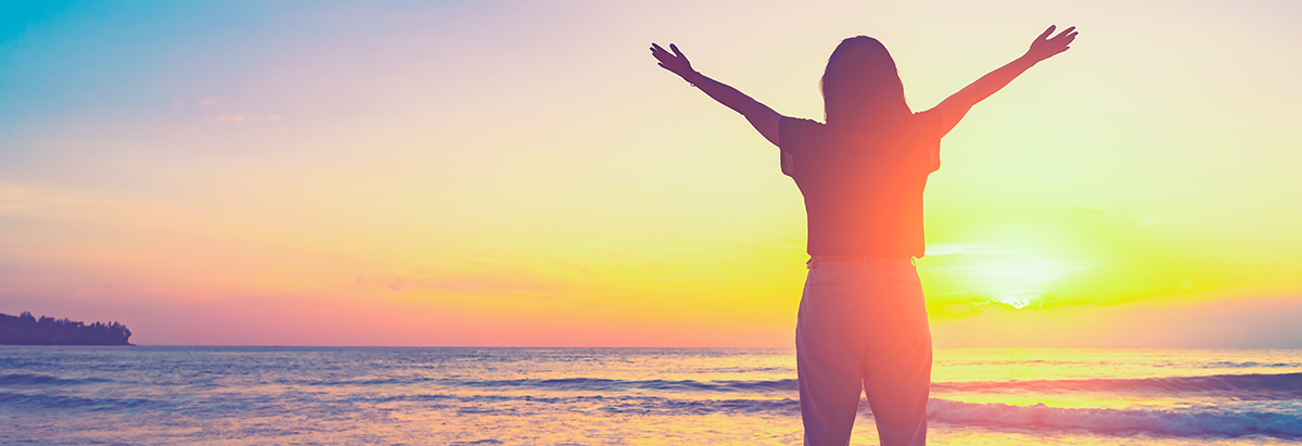 Woman with hands up on sunset sky at beach and island background.